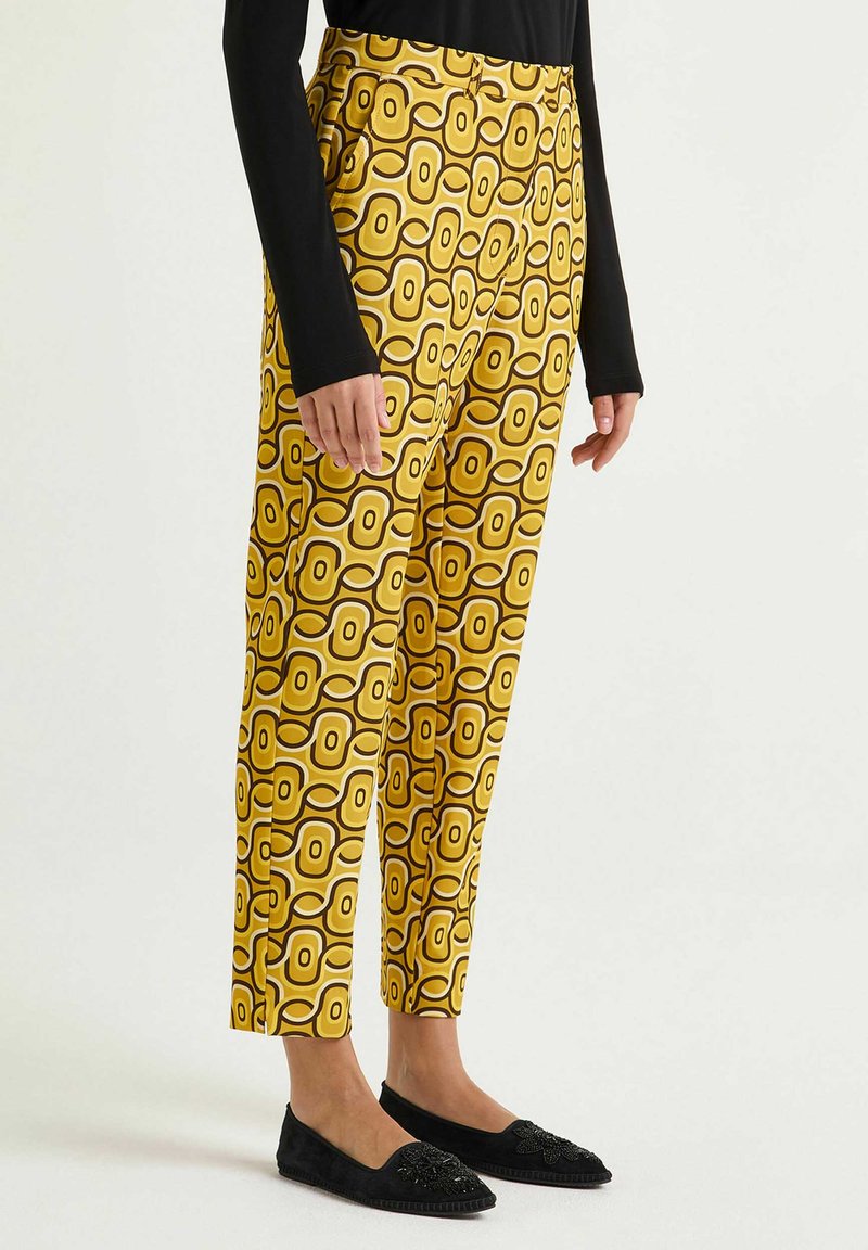 Pantaloni gialli con motivo a esagoni contornati di marrone, taglio sfiancato, realizzati in tessuto liscio, abbinati a ballerine nere.