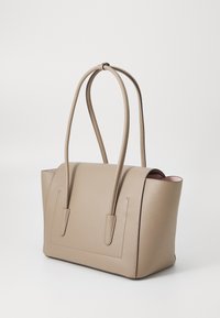 Sac fourre-tout en cuir beige avec deux longues poignées, forme structurée et design minimaliste. Présente un intérieur rose contrasté.