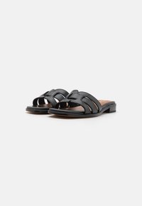Sandali in pelle nera a scivolo con un design aperto sulla punta, multiple cinghie intrecciate, un tacco basso a blocco e una soletta liscia e morbida.