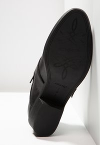 Semelle de chaussure à talon noire avec motif décoratif, nom de marque « Anna Field » et taille 37 visible en dessous.