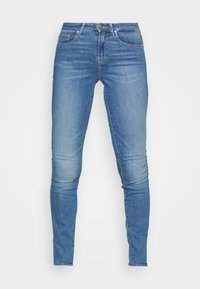 Jeans skinny de mezclilla azul claro con una cintura de altura media, diseño de cinco bolsillos y un ligero desvanecimiento a lo largo de los muslos y las rodillas.