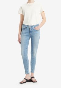 Ljusblå skinny jeans med hög midja, fem fickor och en lätt blekning, i kombination med en vit T-shirt och svarta remsandaler.