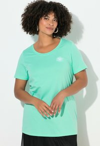 Mátově zelené tričko s kulatým výstřihem a krátkými rukávy, zdobené malým motivem oka na hrudi. Měkká látka s volným střihem.