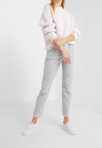 Suéter de color rosa claro con textura de canalé, pantalones de pana gris y zapatillas color crema. El conjunto tiene un corte relajado con una tela texturizada y un diseño casual.