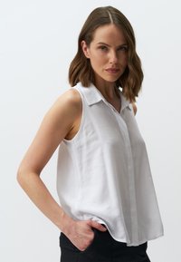 Blusa bianca senza maniche con chiusura a bottoni, colletto e vestibilità rilassata. Realizzata in un tessuto leggero e morbido.