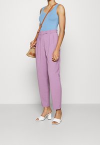 Lichtblauw tanktop, hooggeribde lavendelkleurige broek, witte hoge hakken en een geweven rieten tas met bruine accenten.
