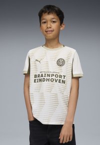 Maglia da calcio bianca e beige chiaro con righe orizzontali, scollatura rotonda e il testo verde "BRAINSPORT EINDHOVEN." Maniche corte.