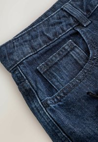 Džíns s tmavomodrou farbou, s jednou zadnou kapsou a pevným šitím. Materiál je hladký s jemnou štruktúrou.