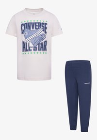 White cotton t-shirt with graphic print of blue sneakers and green stars, paired with dark blue elastic waist jogger pants featuring logo.