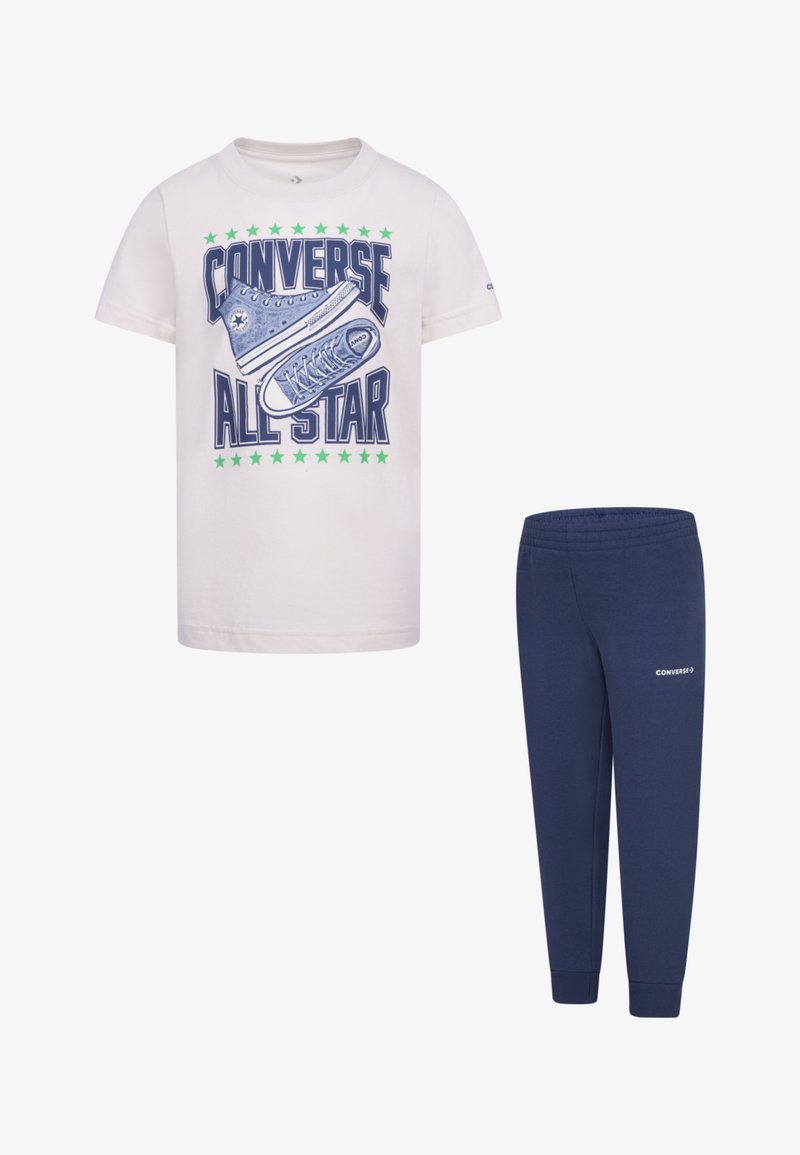 Λευκό T-shirt από βαμβάκι με γραφικό σχέδιο μπλε αθλητικών παπουτσιών και πράσινων αστεριών, σε συνδυασμό με σκούρες μπλε παντελόνες με ελαστική μέση και λογότυπο.