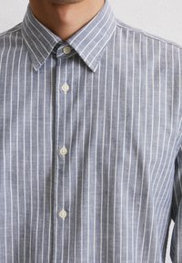 Button-up shirt in light blue fabric with white vertical stripes; features a spread collar and white buttons along the placket.