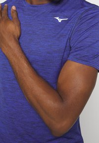 Blå idrottströja i strukturerad, fukttransporterande tyg. Har en vit logotyp på bröstet. Korta ärmar och rundad halsringning.