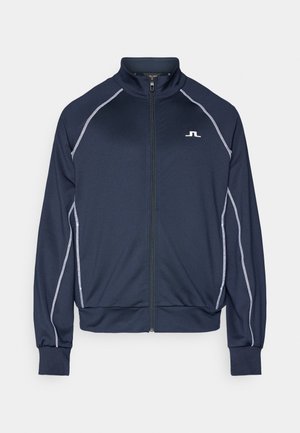 Giacca a zip blu navy con colletto alto. Presenta piping grigio chiaro a contrasto lungo le spalle e le braccia. Tessuto morbido e liscio.