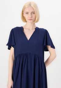 Abito blu navy realizzato in tessuto morbido, con maniche corte a sbuffo, scollatura a V e vita arricciata per una vestibilità rilassata.