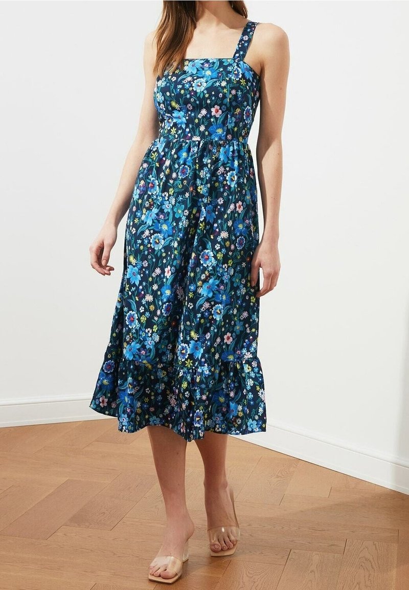 Blumenkleid in Dunkelblau mit verstellbaren Trägern, tailliertem Oberteil und rüschendem Saum. Es hat mehrfarbige Blumen und eine glatte Stofftextur.