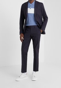 Mörkblå kostym för män med slim-fit-design, kombinerad med en ljusblå randig polotröja och vita sneakers. Slät tyg och modern siluett.