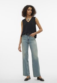 Black sleeveless top with a V-neck, paired with light blue wide-leg jeans and black flats. A decorative silver necklace accents the outfit.