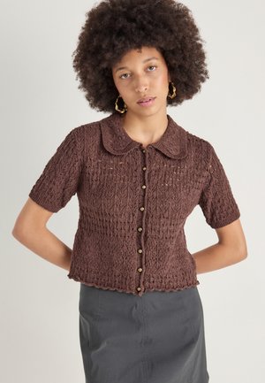 Gilet short en tricot marron à manches courtes avec un col, présentant un tissage ouvert texturé et une fermeture à boutons sur le devant.