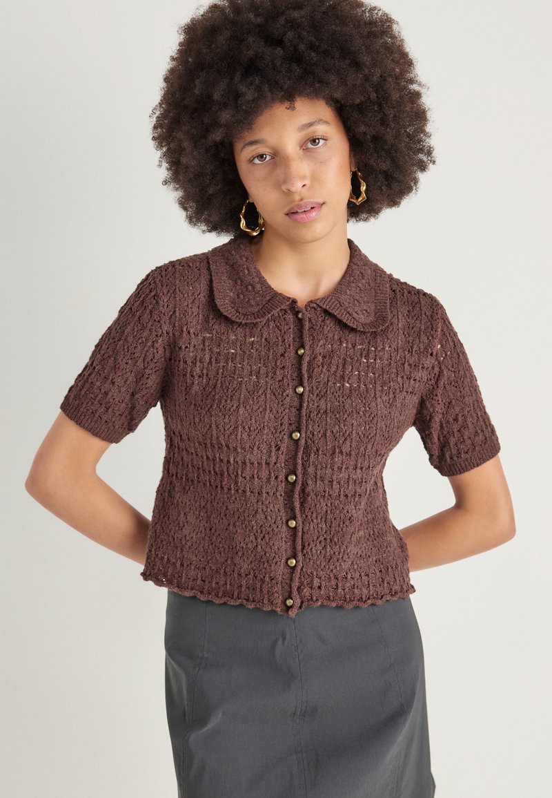 Καφέ πλεκτό κοντομάνικο καρδινοποίημα με γιακά, διαθέτοντας υφή ανοιχτού πλέγματος και κλείσιμο με κουμπιά μπροστά.