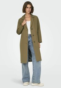 Cappotto lungo verde oliva con colletto a punte, bottoni frontali e tasche laterali; foderato con stampa leopardata. Abbinato a jeans a gamba larga.