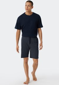 Camiseta de cuello redondo color marino con bolsillo delantero, combinada con pantalones cortos marinos de longitud a la rodilla que presentan un pequeño patrón de lunares blancos.