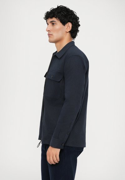 Navy blue jacket made of textured fabric, featuring a zip front, collared neckline, and a chest pocket with button closure.