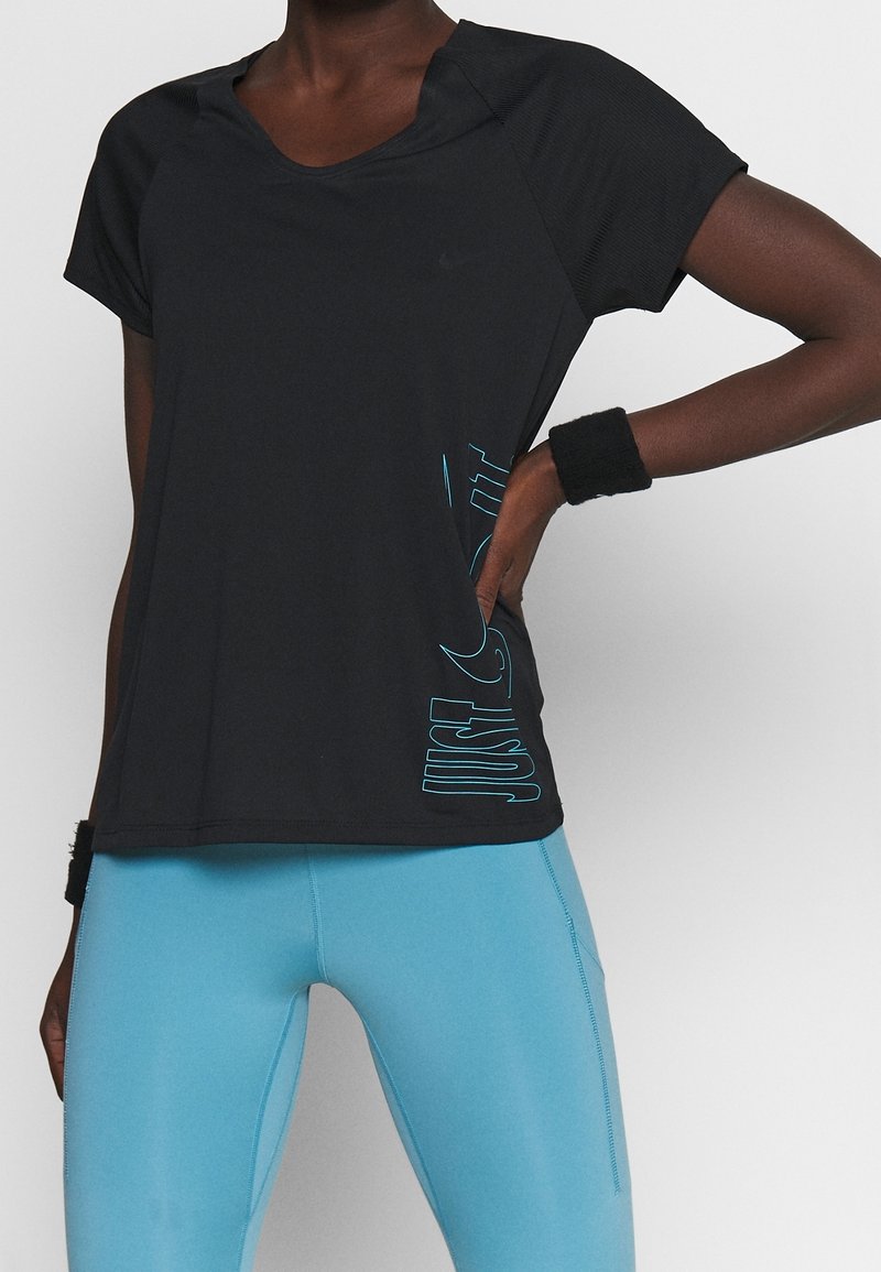 Mujer que lleva una camiseta deportiva negra de manga corta con el texto lateral "SÓLO HAZLO" y leggins azul claro, con muñequeras negras en ambas muñecas.