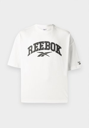 Valkoinen puuvillainen T-paita lyhyillä hihoilla, jossa on musta "REEBOK" -logo ja pieni Reebok-logoakseli vasemmassa hihassa.