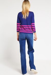 Marinblå tröja med rosa ränder, trekvartsärmar; kombinerad med ljusblå utsvängda jeans. Mjuk textur och avslappnad passform.