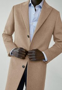 Beige wollen jas met een op maat gemaakt ontwerp, enkele knoopsluiting en notch revers. Draag het over een lichtblauw gestreept overhemd.