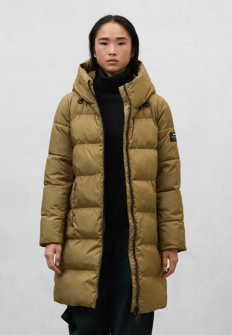 Manteau long et gonflé en vert olive avec capuche, comportant des sections matelassées, un zip frontal et des accents noirs sur les manches.