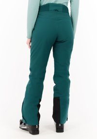 Teal skibroek met een rekbare tailleband, taps toelopende benen en zwarte accenten aan de zoom. De stof lijkt glad en waterafstotend te zijn.