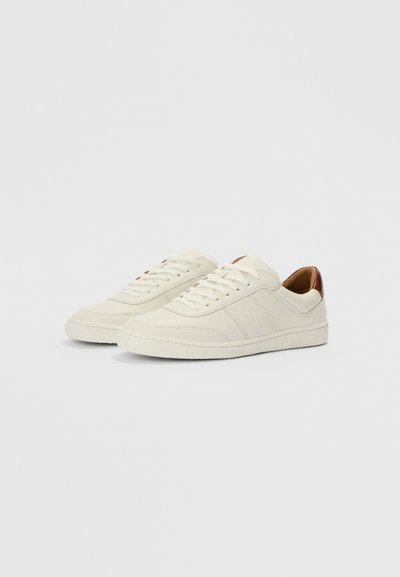 Balti ādas sporta apavi ar teksturētām panelēm, apaļu purngalu un brūniem ādas akcentiem papēdī. Aprīkoti ar plakanām auklām un gumijas zolīti.