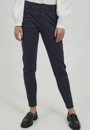 Námornické slim-fit kalhoty vyrobené z elastické látky, s hladkým povrchem, poutky na opasek a zipem s knoflíkovým zapínáním. Nosené s černými mokasínami.