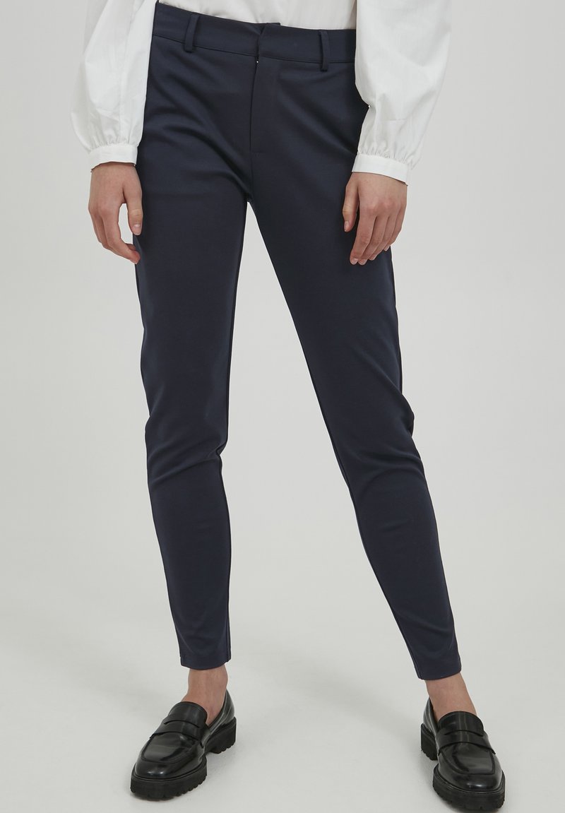 Námornické slim-fit kalhoty vyrobené z elastické látky, s hladkým povrchem, poutky na opasek a zipem s knoflíkovým zapínáním. Nosené s černými mokasínami.