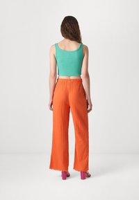 Un crop top turquoise ajusté et côtelé associé à un pantalon orange texturé ample avec des ourlets effilochés et des sandales à talons roses.