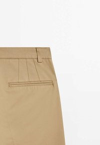 Pantalon kaki avec une poche passepoilée au dos et des passants de ceinture, présenté sur un fond blanc uni.