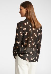 Blusa nera e trasparente con stampa floreale in crema e rosa, polsini a bottoni e orlo arrotondato. Tessuto liscio e vestibilità comoda.