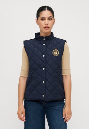 Gilet blu navy trapuntato con colletto alto, bottoni a scatto argentati e toppa logata. Realizzato in tessuto liscio e leggero; senza maniche.
