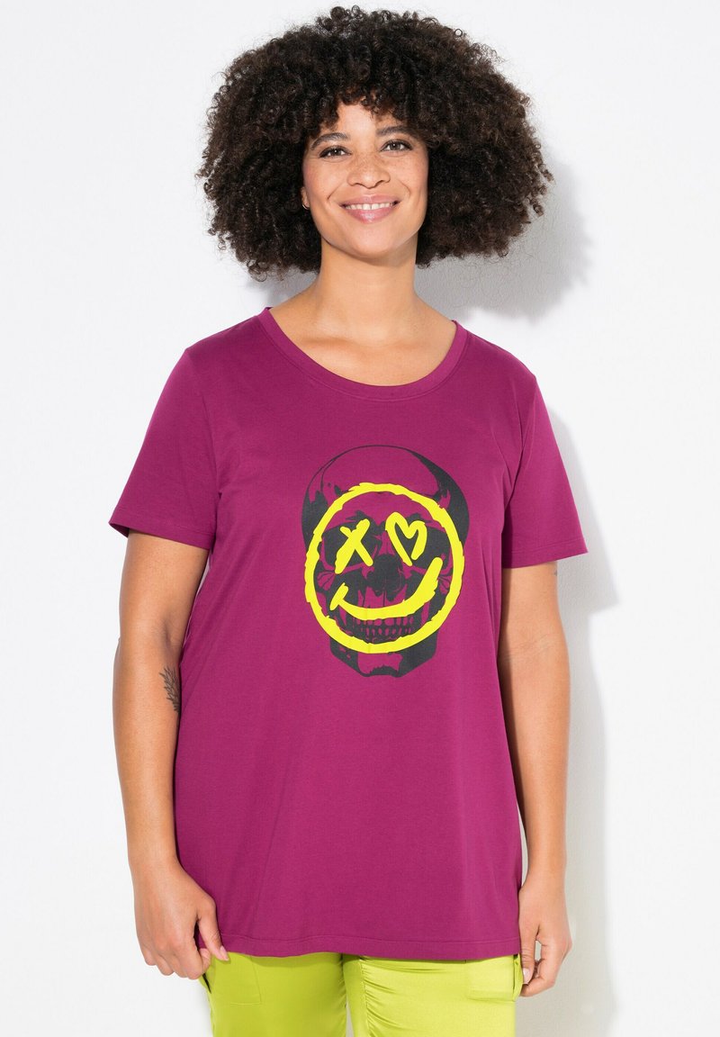 Lilla bomulds T-shirt med en sort og gul skull smiley grafik i midten. Korte ærmer og rund halsudskæring.