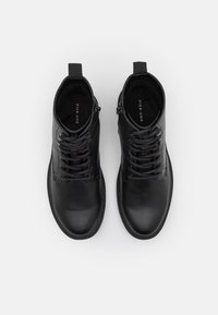 Botas de cuero negro hasta el tobillo con punta redonda, cordones en la parte delantera y cremalleras en los lados. Textura suave con un diseño minimalista y suelas acolchadas.