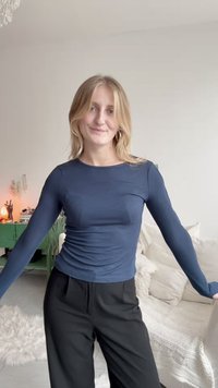 Mørkeblå langermet topp laget av et glatt stoff, med en tettsittende design og rund hals, kombinert med svarte plisserte bukser.