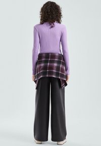 Fioletowy prążkowany top z długim rękawem, nałożony na czarno-fioletową koszulę w kratę, zestawiony z szerokimi czarnymi spodniami i beżowymi butami. Widok od tyłu.