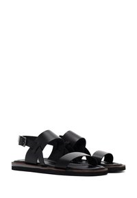 Black leather sandals featuring wide straps, an adjustable ankle buckle, and a flat sole with a brown accent along the edge.