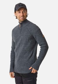Sweater zippé en charbon avec texture côtelée, manches longues et fermeture éclair d'un quart de longueur. Présente un patch logo sur le bras gauche.