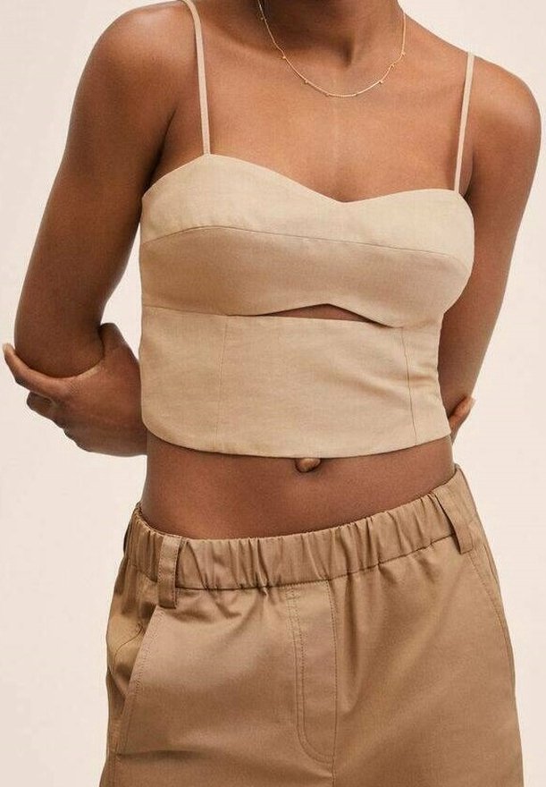 Top cropped beige avec fines bretelles et décolleté arrondi, présentant un détail de découpe à l'avant. Associé à un pantalon beige ample.