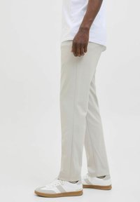 Světle šedé kalhoty s přímým střihem, se subtilním bočním prošitím, spárované s bílými teniskami a bílým tričkem.