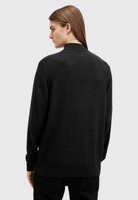 Maglione nero in maglia spessa con collo alto, maniche lunghe e polsini a coste. Tessuto liscio con una vestibilità leggermente rilassata.