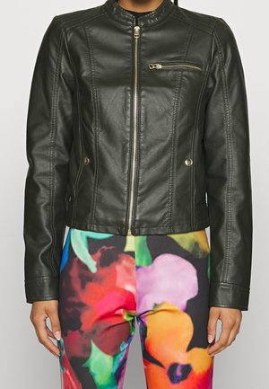 Schwarze Kunstlederjacke mit Frontreißverschluss und Reißverschlusstasche auf der Brust, getragen über lebhaft geblümter Hose.