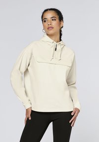 Cream-colored hooded pullover made of ribbed fabric, featuring a front pocket, adjustable drawstrings, and long sleeves. Black accents on hardware.